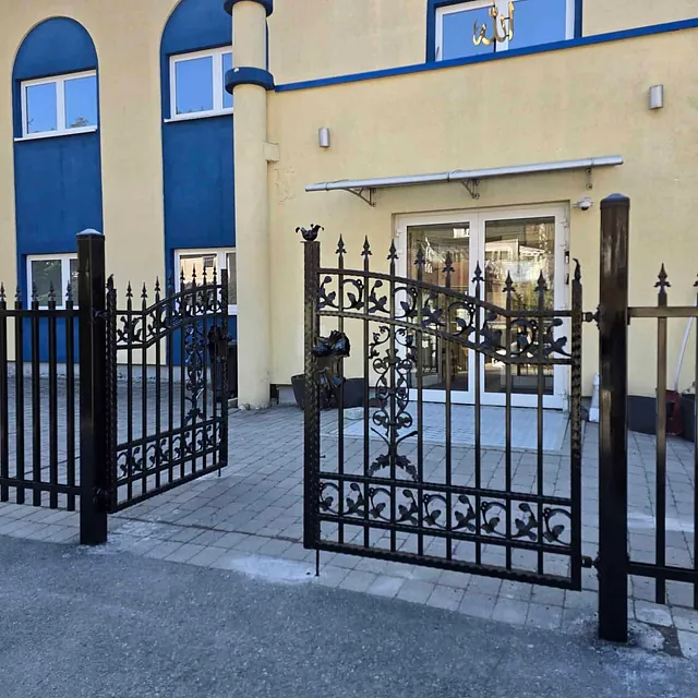 Dekorativ smijernsport med spir og mønster foran gul bygning med blå detaljer.