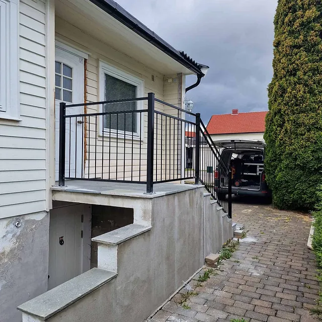 Inngangsparti med trapp og ny sort rekkverk montert utenfor hvitt hus med kjellerdør under.