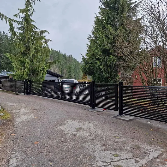 Hvit bolig med lang sort skyveport og flere seksjoner i metall foran oppkjørsel.